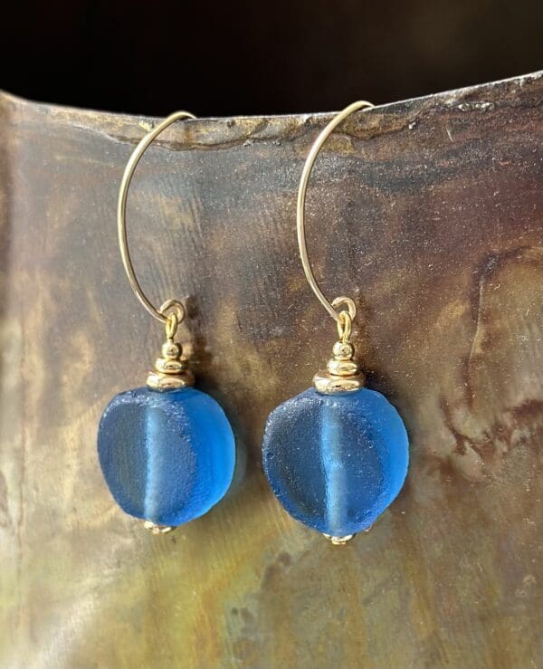 A pair of blue earrings hanging on top of a metal surface.