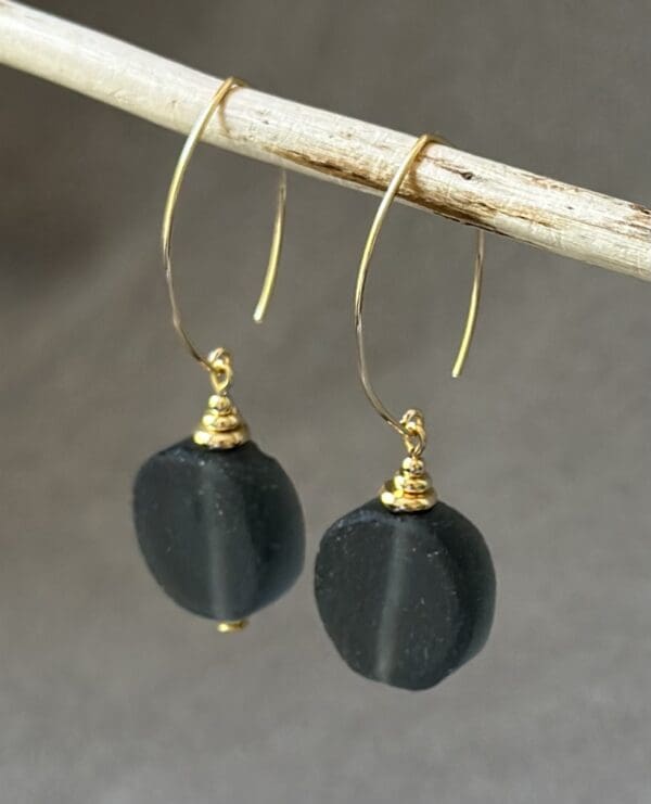 A pair of black earrings hanging on top of a stick.