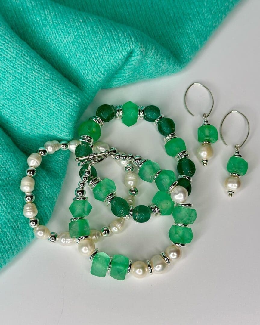 A green bracelet and earrings are sitting on top of a white cloth.