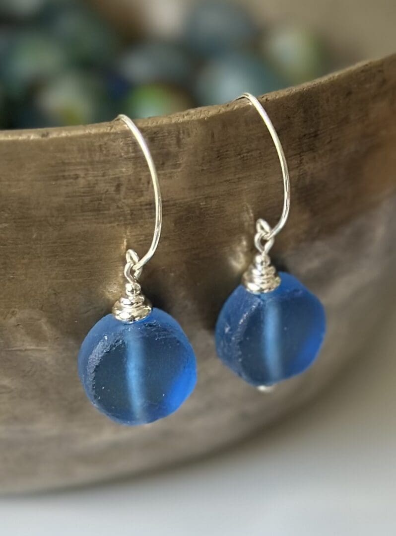 A pair of blue earrings sitting on top of a wooden bowl.