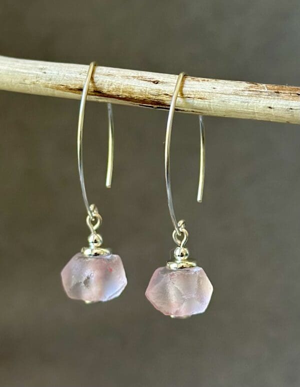 A pair of pink earrings hanging on a stick.