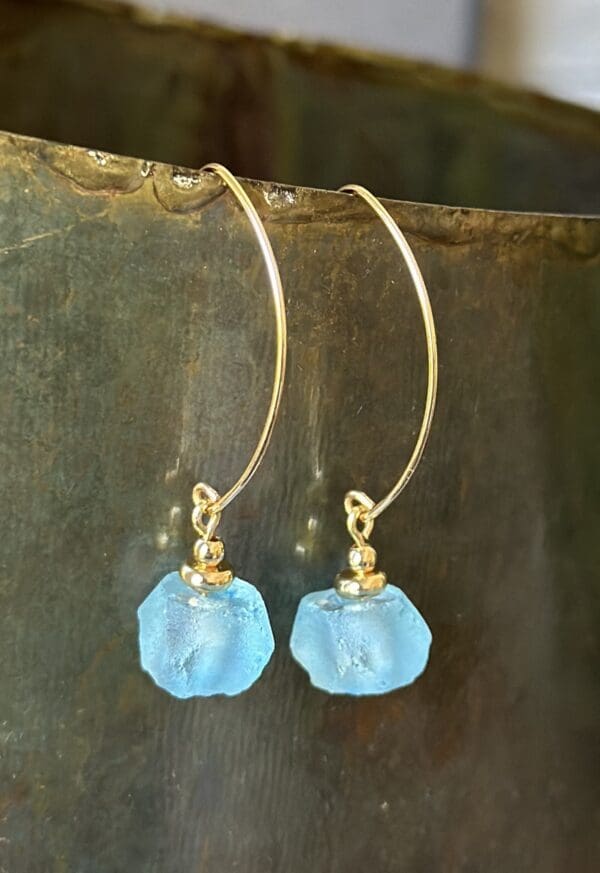 A pair of blue earrings hanging on top of a metal surface.