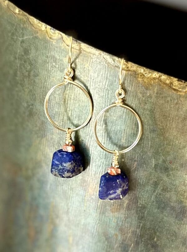 A pair of earrings with blue stones hanging from them.