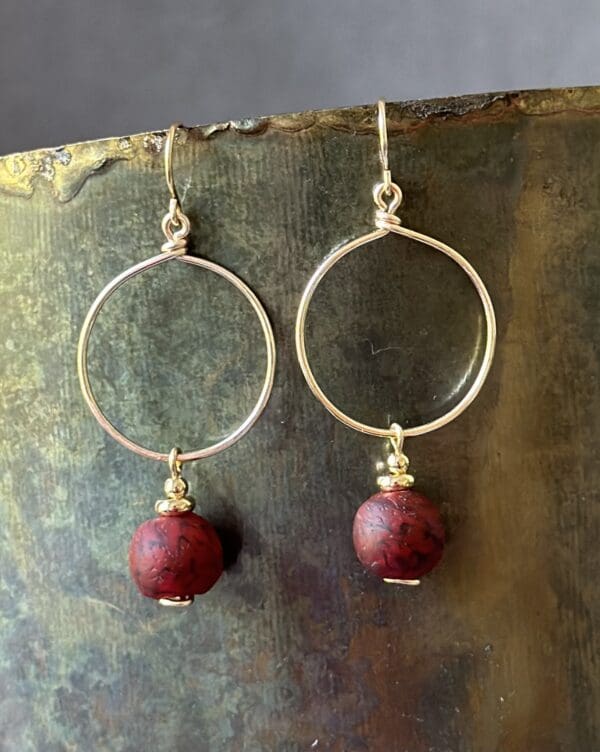 A pair of earrings with red beads hanging from them.