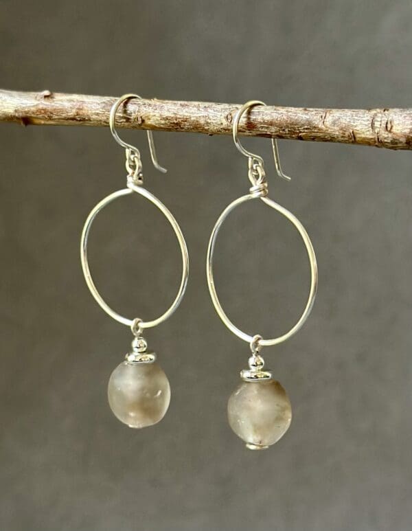 A pair of silver earrings hanging from a tree branch.