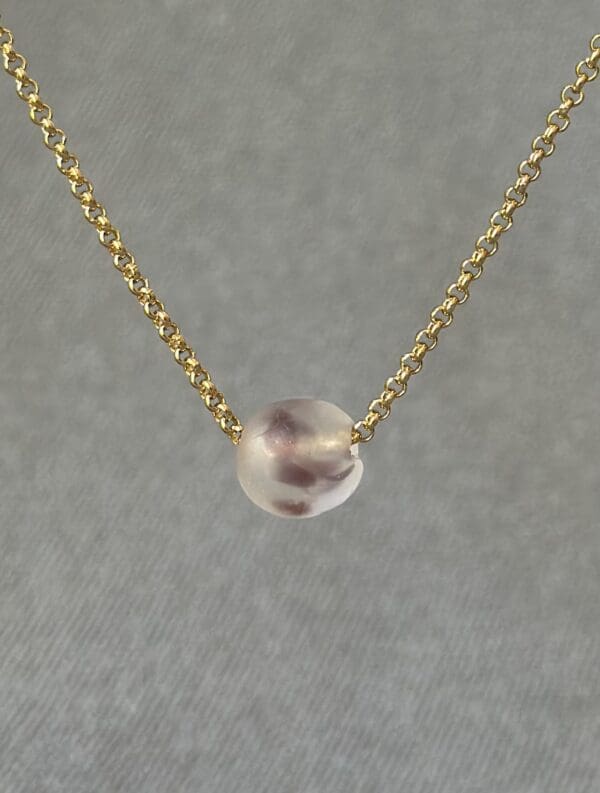 A gold chain with a small glass bead on it.