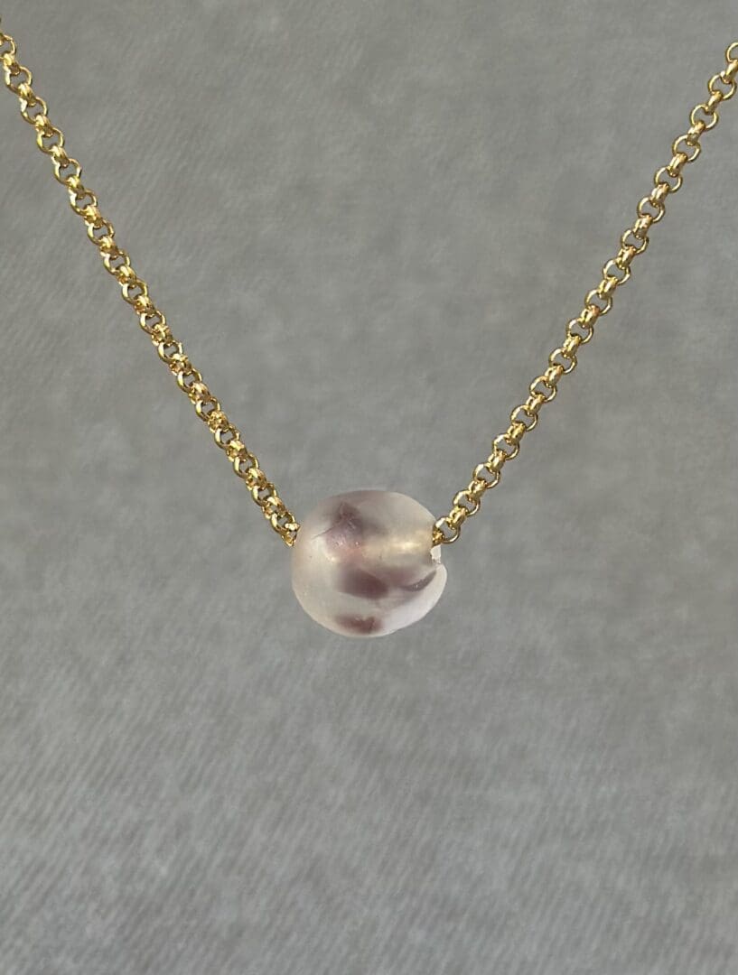 A gold chain with a small glass bead on it.