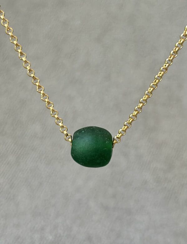 A green bead is on the chain of a necklace.