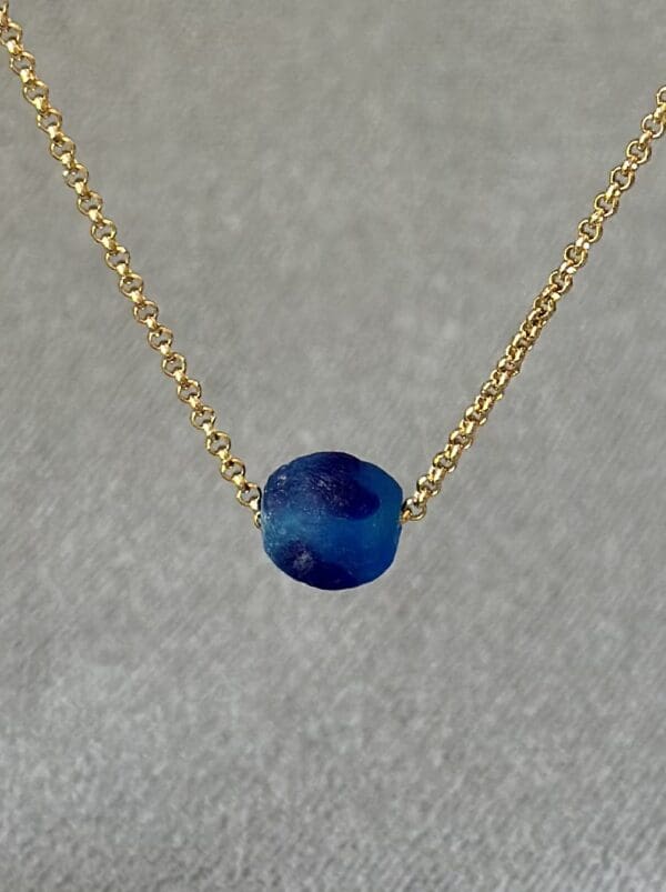 A blue bead is on the chain of a gold necklace.