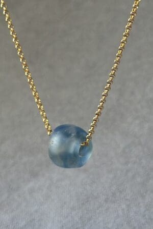 A blue bead is on the chain of a gold necklace.