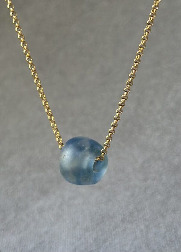 A blue bead is on the chain of a gold necklace.